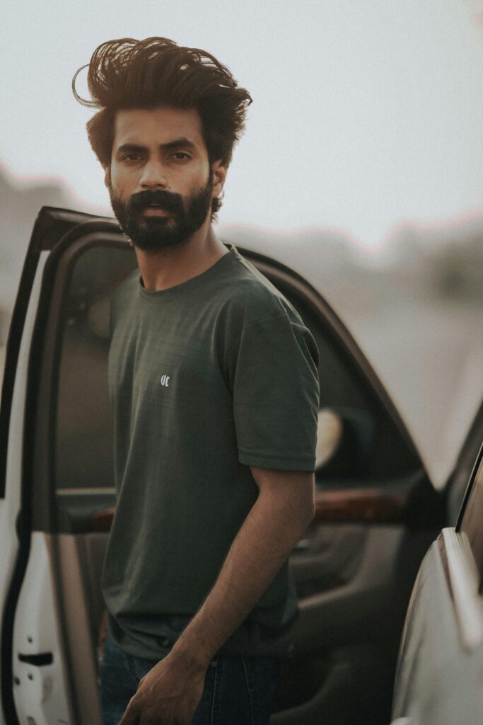Young bearded man standing by a car in Abu Dhabi, captured in a warm and moody setting.